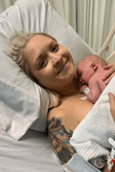 Older new mom in hospital bed smiling and holding newborn baby. 