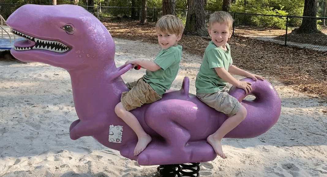 Two school-aged boys ride on a purple dinosaur on springs.