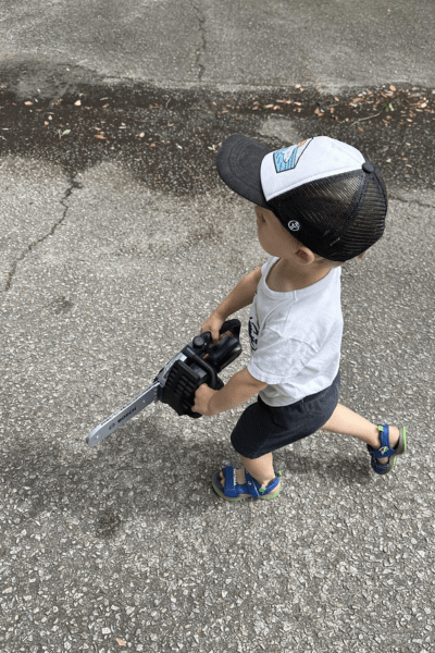 a little boy walks on pavement with a toy chainsaw